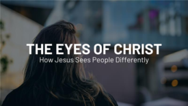 A person with long hair is seen from behind, looking toward a blurred cityscape. Text on the image reads: ‘The Eyes of Christ’ and ‘How Jesus Sees People Differently.’