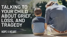 An adult and a young boy sit side by side outdoors on a ledge, both facing away as the adult leans forward in a posture of concern or reflection. Text on the image reads: ‘Talking to Your Child About Grief, Loss, and Tragedy.’ The Hope for the Heart logo appears below.