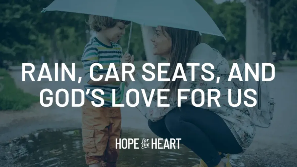 A woman holding an umbrella kneels beside a young child standing near a puddle, both smiling as they talk. Text on the image reads: ‘Rain, Car Seats, and God’s Love for Us.’ The Hope for the Heart logo appears at the bottom.
