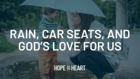 A woman holding an umbrella kneels beside a young child standing near a puddle, both smiling as they talk. Text on the image reads: ‘Rain, Car Seats, and God’s Love for Us.’ The Hope for the Heart logo appears at the bottom.